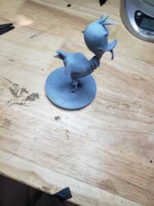 A stylized Road Runner figurine, reminiscent of the classic Looney Tunes character, 3D printed in gray resin with a circular base reading “Flip The Switch.”