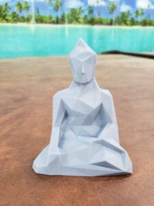 A geometric low-poly Buddha statue in gray resin, 3D printed by PlastiForge3D, featuring clean angular facets and a modern aesthetic.