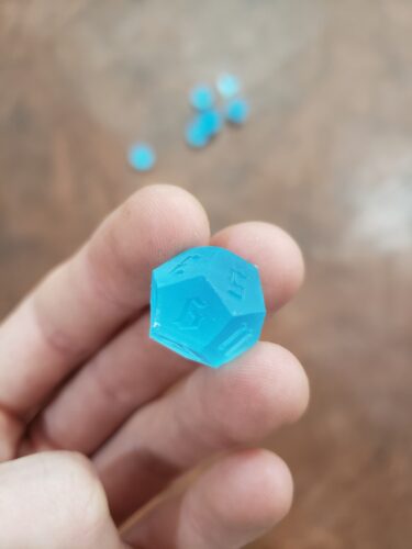 A translucent blue, 3D-printed polyhedral dice created by PlastiForge3D, showing custom engraving and varying numbers of sides for tabletop gaming.