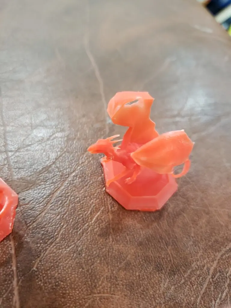 A small, orange dragon miniature, 3D printed by PlastiForge3D for tabletop gaming, showcasing fine detail and SLA resin quality.