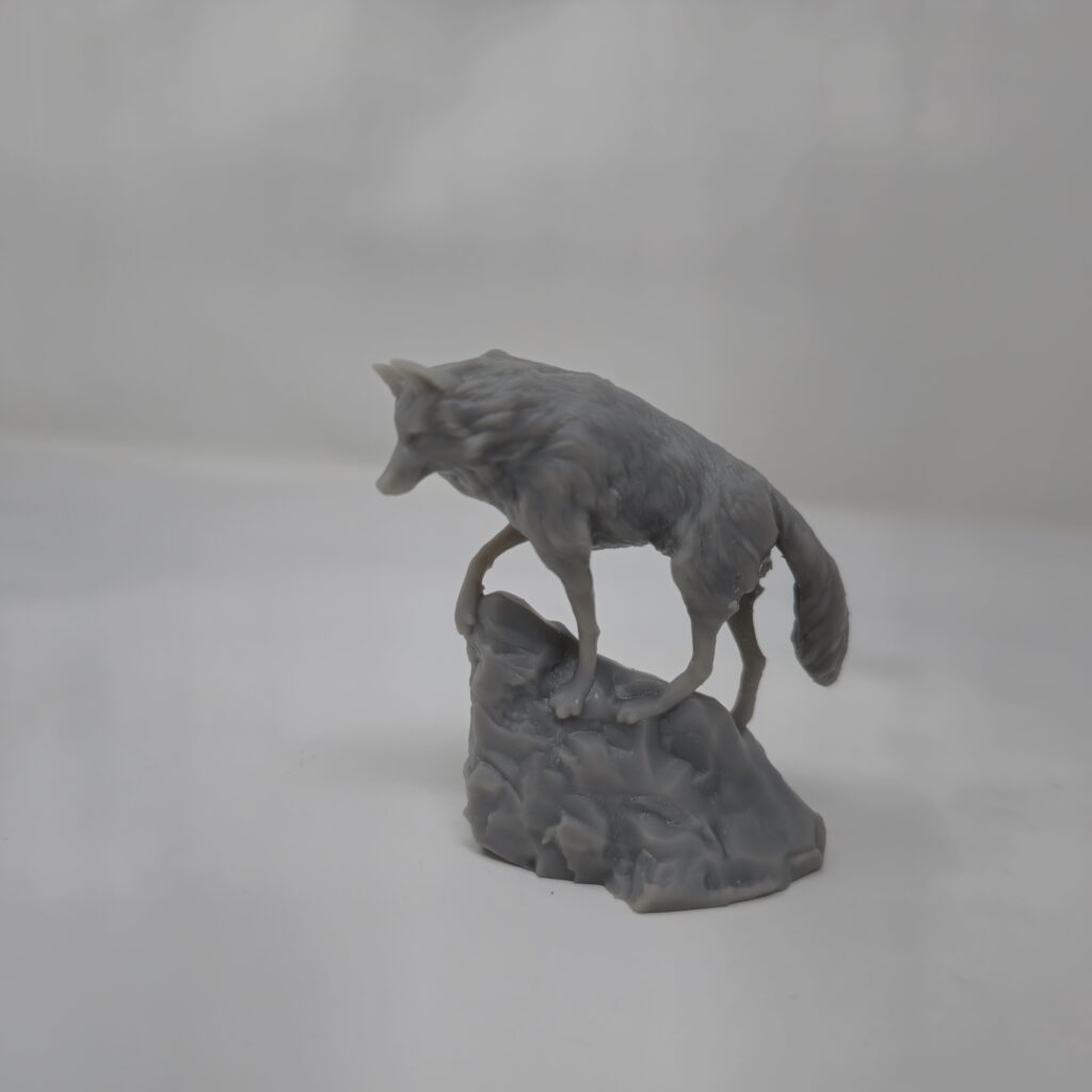 A highly detailed Snow Wolf figure in gray resin, 3D printed by PlastiForge3D and perched atop a rocky base.