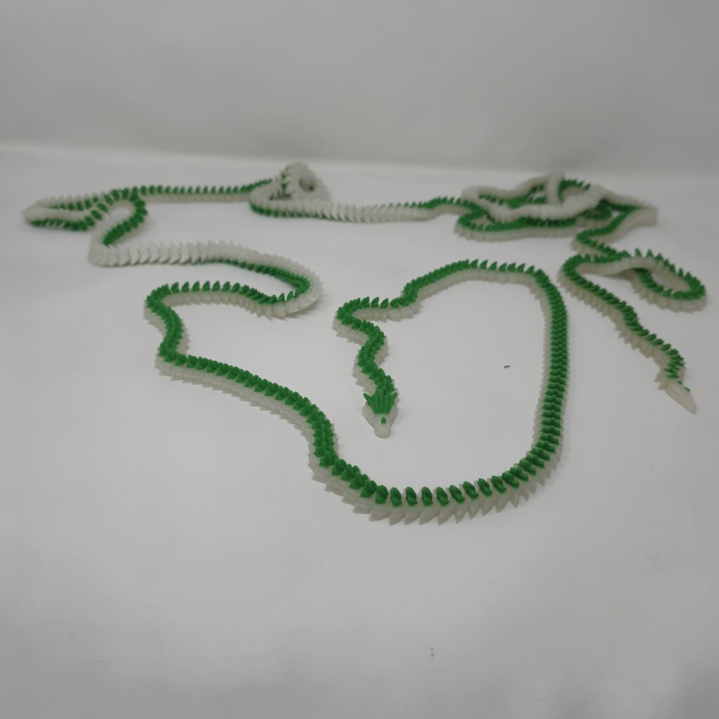 A sprawling, 10-foot 3d printed dragon figurine featuring green and translucent segments, fully 3D printed using FDM technology and laid out on a white surface.