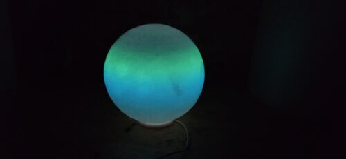 A glowing moon lamp radiating greenish-blue light in a dark room, 3D printed with luminescent filament for a captivating nighttime effect.