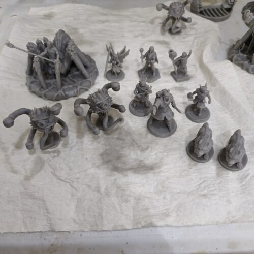A collection of fantasy tabletop miniatures 3D printed in gray resin by PlastiForge3D, featuring heroes, monsters, beholders, and a spider-like boss creature.