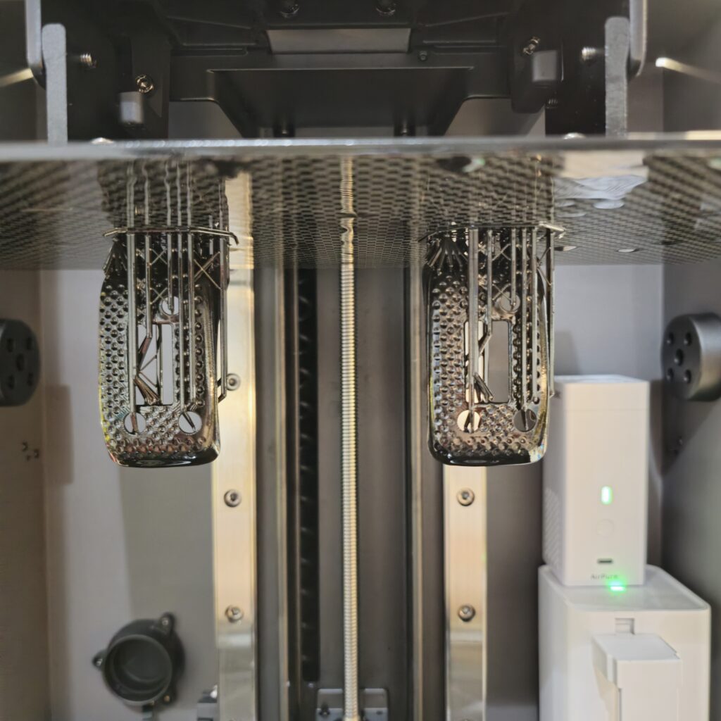 Two custom 3D printed ImmersionRC module covers still attached to a resin printer build plate, showcasing the support structures and printing process.