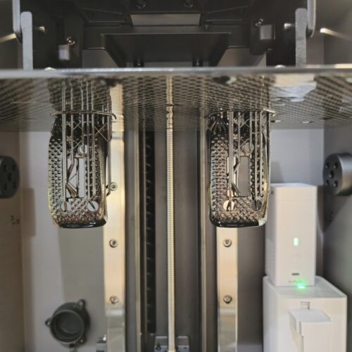 Two custom 3D printed ImmersionRC module covers still attached to a resin printer build plate, showcasing the support structures and printing process.