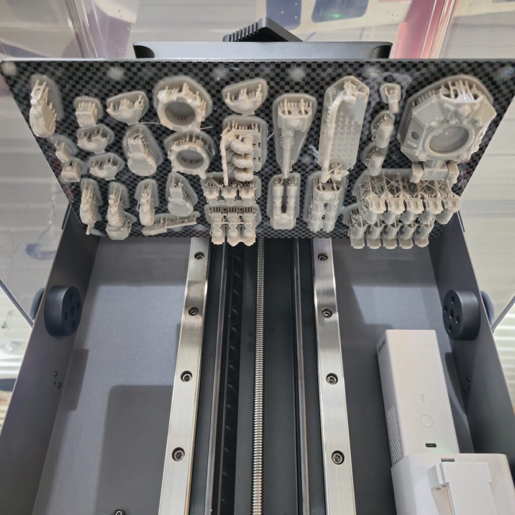 A full build plate of detailed resin-printed parts for a Gladiator tank model from the Warhammer universe, shown attached to a 3D printer.