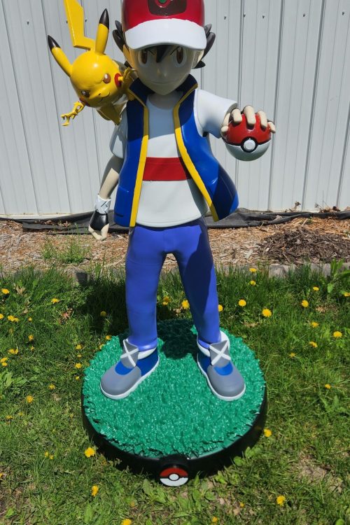 Life size 3D printed and painted custom statue of Ash Ketchum holding a Pokéball with Pikachu on his shoulder, standing on a custom base outdoors.